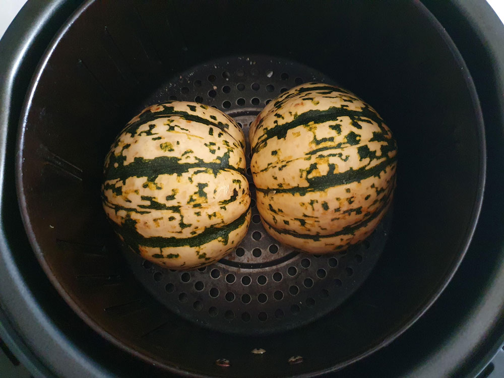 Uncooked acorn squash halves in the air fryer basket