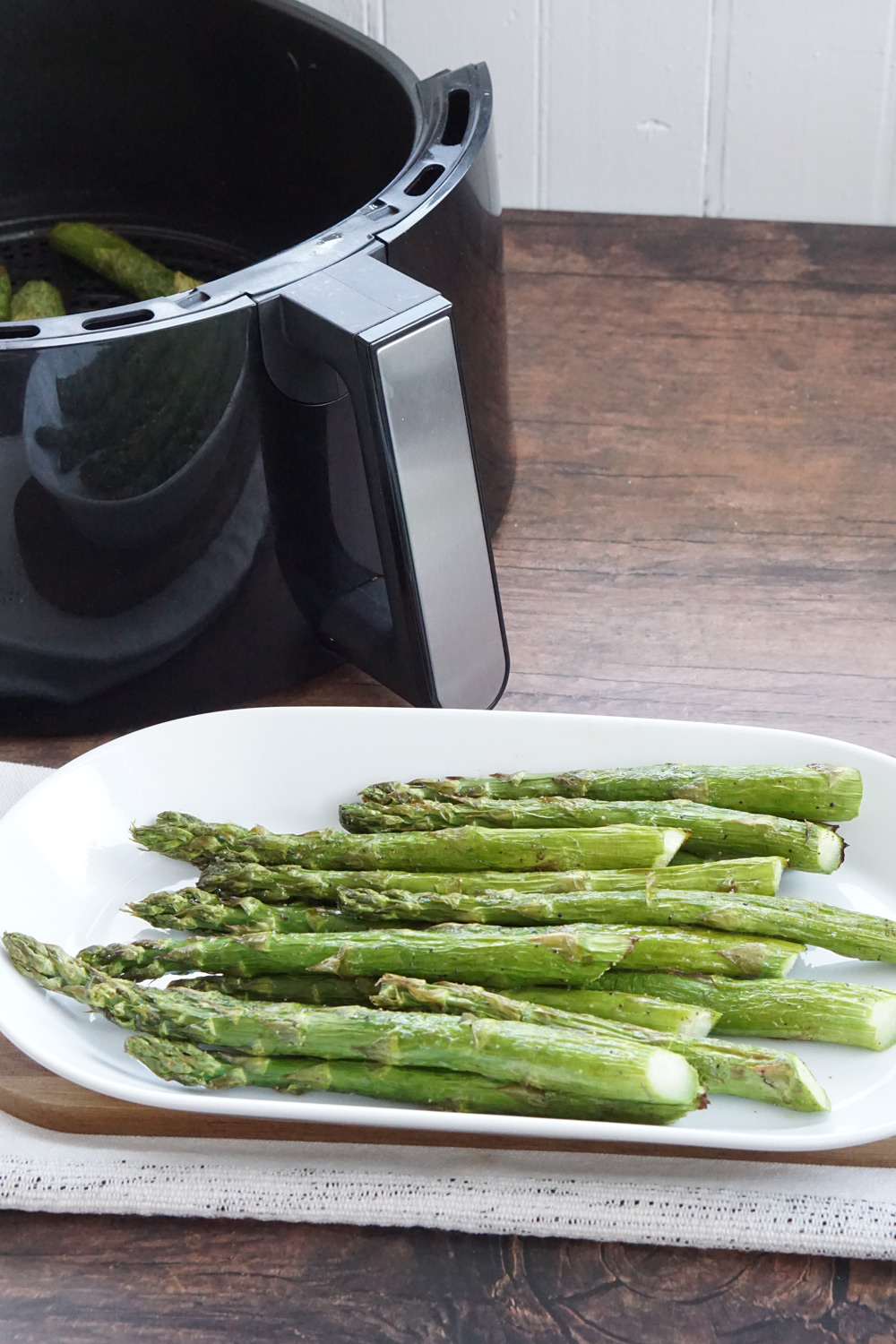 A plate of cooked asparagus with the air fryer basket in the background