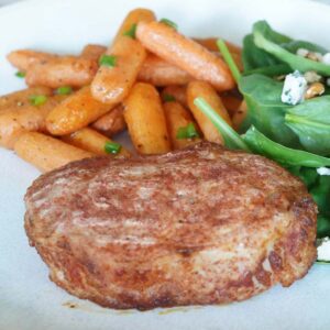A thick pork chop on a plate with salad and carrots